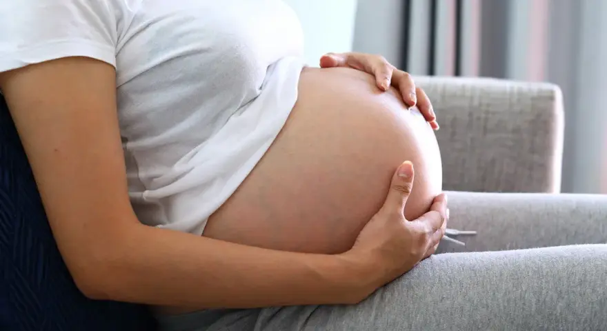 Kobieta w ciąży trzyma dłonie na brzuchu, zastanawiając się, jak przyspieszyć poród.