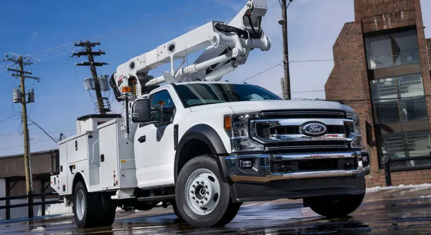 Biały Ford F650 z podnośnikiem koszowym gotowy do pracy przy liniach energetycznych.