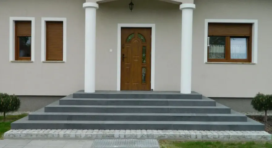 Elegancka, zewnętrzna klatka schodowa w domu jednorodzinnym prowadzi do brązowych drzwi z witrażem.