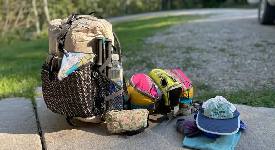 Ready for adventure! This ultralight backpacking gear list includes a tan pack, colorful stuff sacks, trekking poles, a water bottle, and a hat.