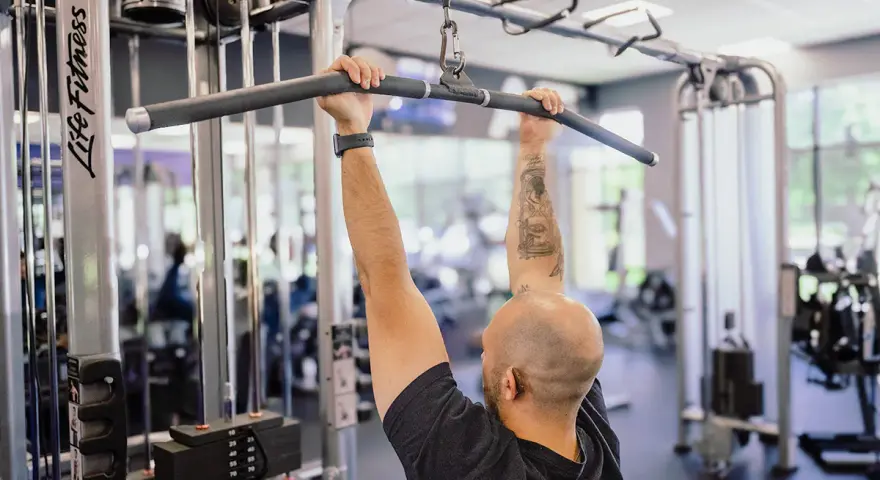 Man med tatueringar utför enarms latsdrag på ett gym.