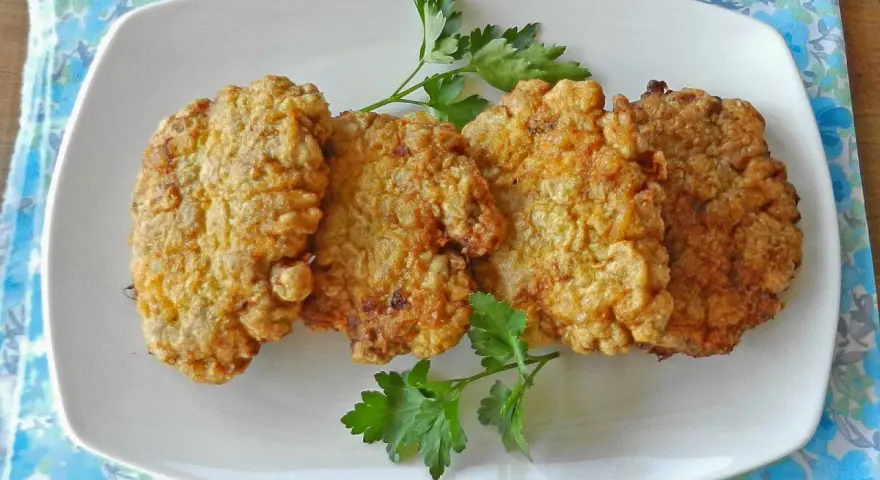 Cuatro filetes rusos dorados y crujientes servidos en un plato blanco con perejil.