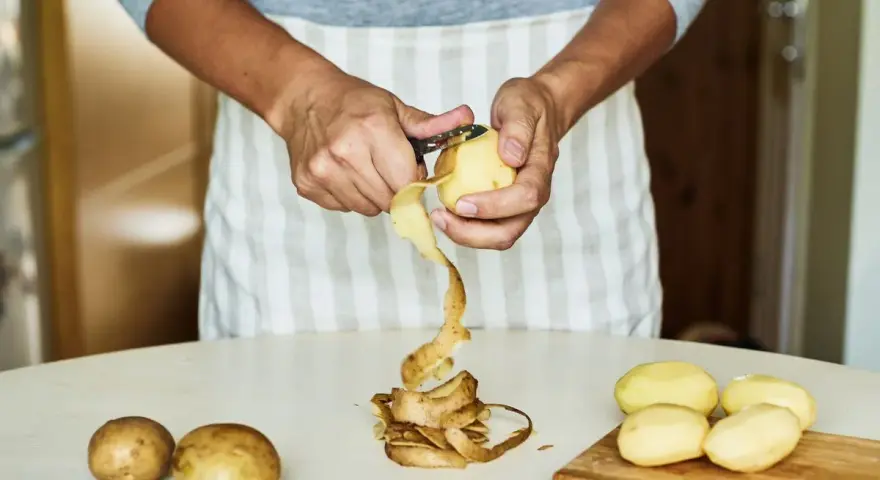 Mani che sbucciano patate per la cottura. Il tempo di cottura patate lesse senza buccia è breve.