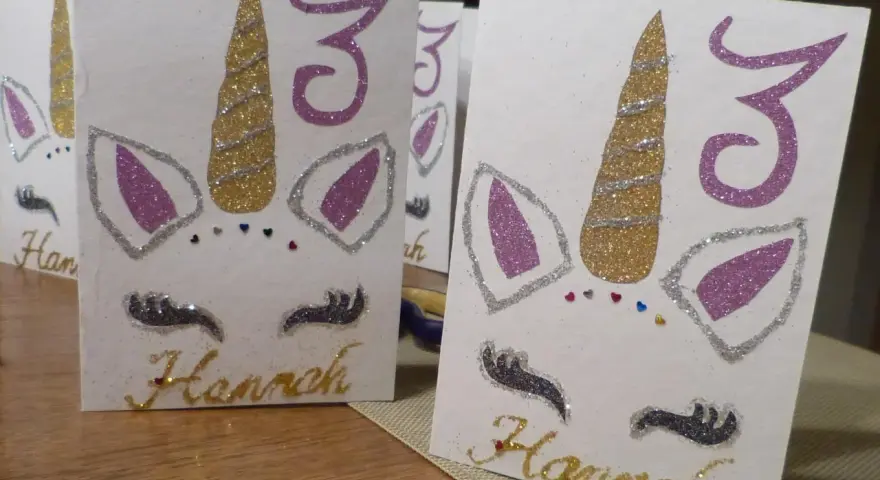 Glitzernde Einhorn-Einladungen zum 3. Geburtstag basteln. Hannahs Name ist in Goldbuchstaben geschrieben.