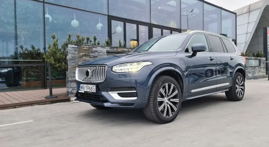 Elegancki, ciemnoszary Volvo XC90 T8 z nowoczesnymi światłami LED stoi przed budynkiem z dużymi, przeszklonymi oknami.