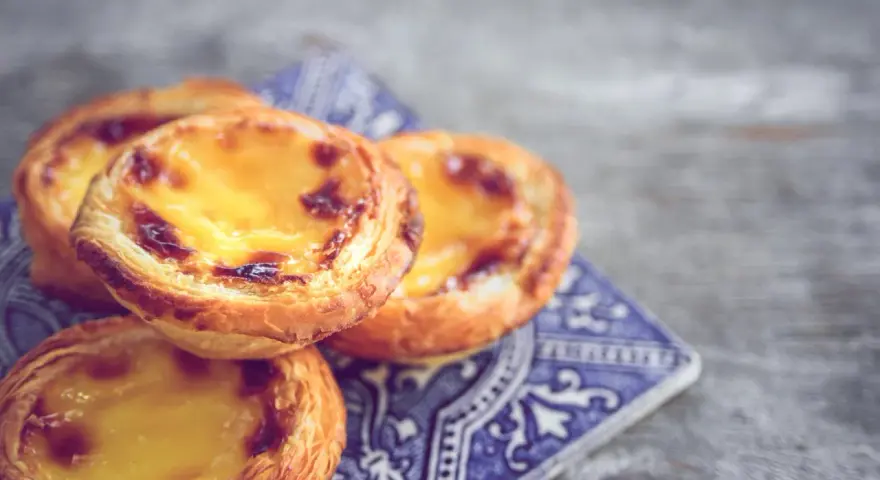 Ein Stapel goldbrauner, karamellisierter Pastel de Nata auf einer blauen Kachel.