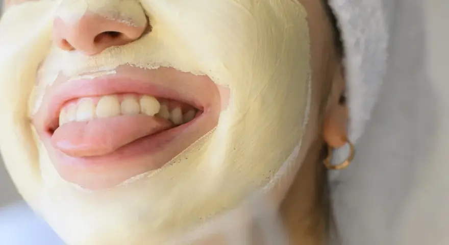 Una mujer se divierte con una mascarilla facial amarilla, sacando la lengua.