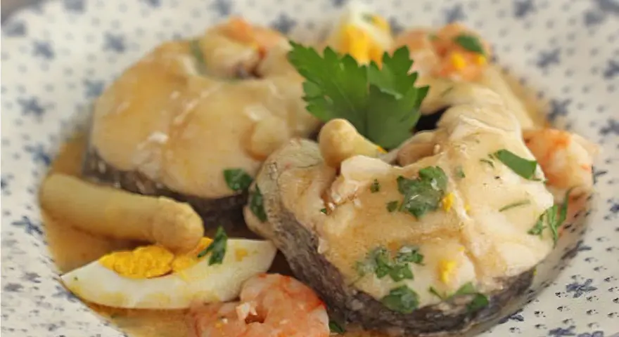 Merluza a la vasca con gambas, huevo duro y perejil, servida en un plato con diseño floral.