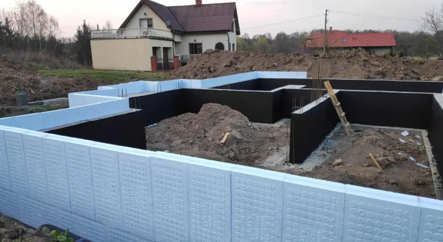 Budowa domu: jak ocieplić fundament styropianem. Widoczne elementy izolacji fundamentów, zbrojenia i ziemia.