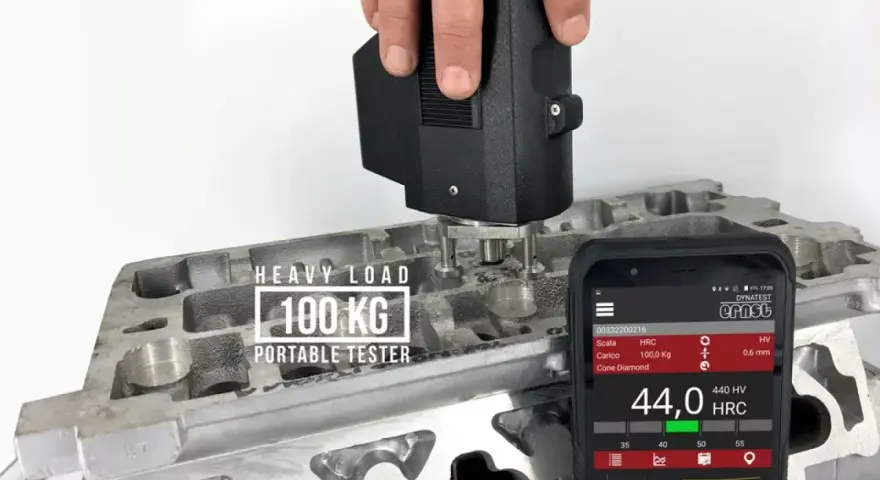 Przenośny tester z obciążeniem 100 kg mierzy twardość materiału, pokazując wyniki na skali twardości na ekranie smartfona.