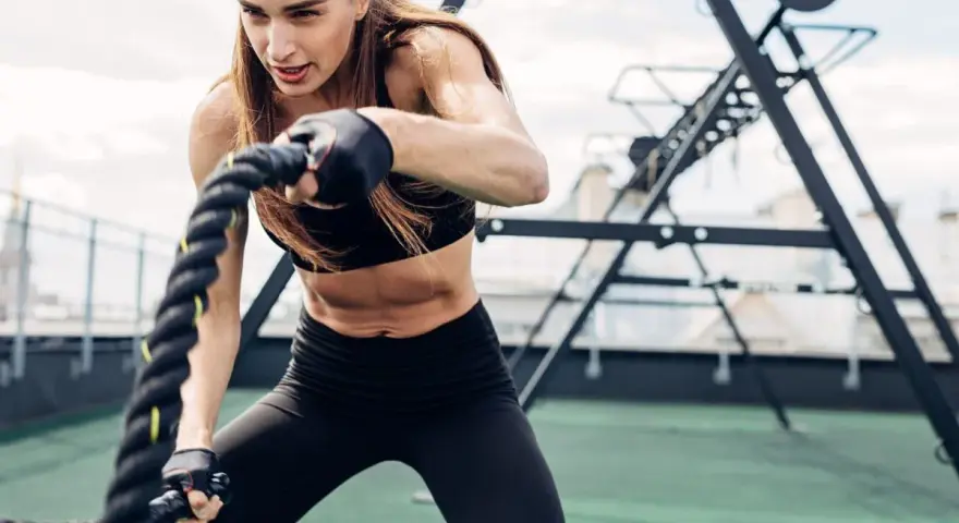 Kobieta wykonuje trening obwodowy z linami battle rope. Intensywny wysiłek buduje siłę i wytrzymałość.