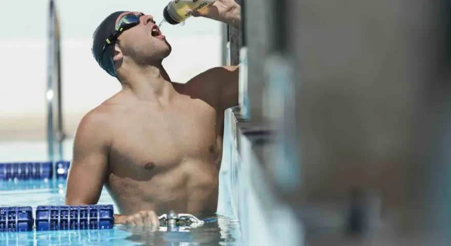 Un nageur en bonnet et lunettes boit dans une bouteille, prêt à apprendre comment nager.