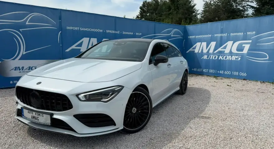 Biały Mercedes na tle niebieskiego banera AMAG Auto Komis. Idealny do akcje serwisowe Mercedes.