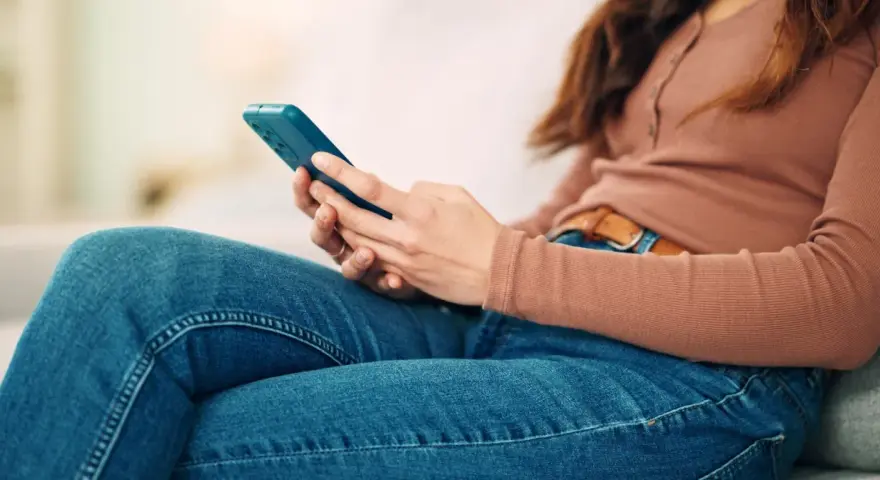 Kobieta w dżinsach i bluzce z długim rękawem trzyma telefon. To może być obraz skutków zbyt długiego korzystania z telefonu.