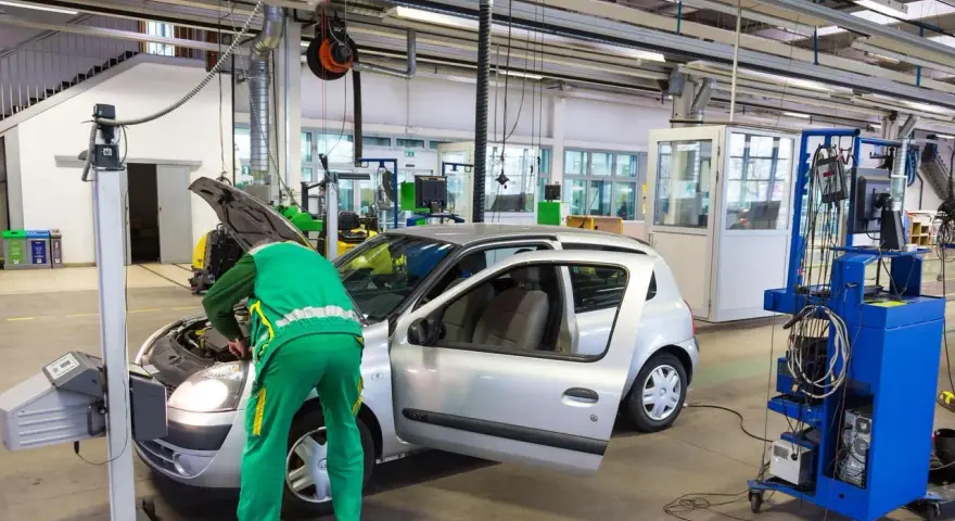 Un meccanico in tuta verde controlla un'auto argentata in un'officina, forse per un controllo secondo l'articolo 80 del codice della strada.