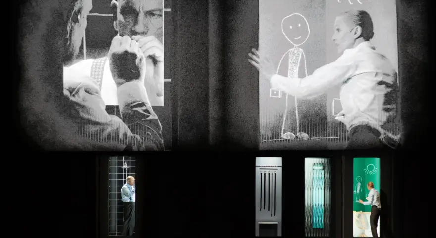 Scena teatralna z projekcjami. Na górze czarno-białe obrazy mężczyzn i kobiety rysującej słońce. Na dole, w oknach, samotność pól bawełnianych, mężczyzna w klatce, przedmioty i kobieta rysująca.