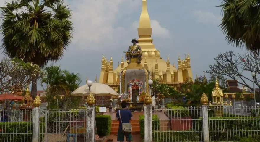Złota stupa Pha That Luang, symbol stolicy w Wientianie, otoczona palmami i zielenią.