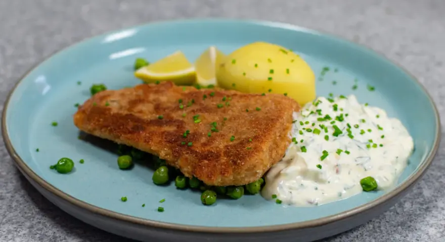Panerad fisk med kokt potatis, ärtor och en krämig kall sås till fisk, garnerad med gräslök och citronklyftor.