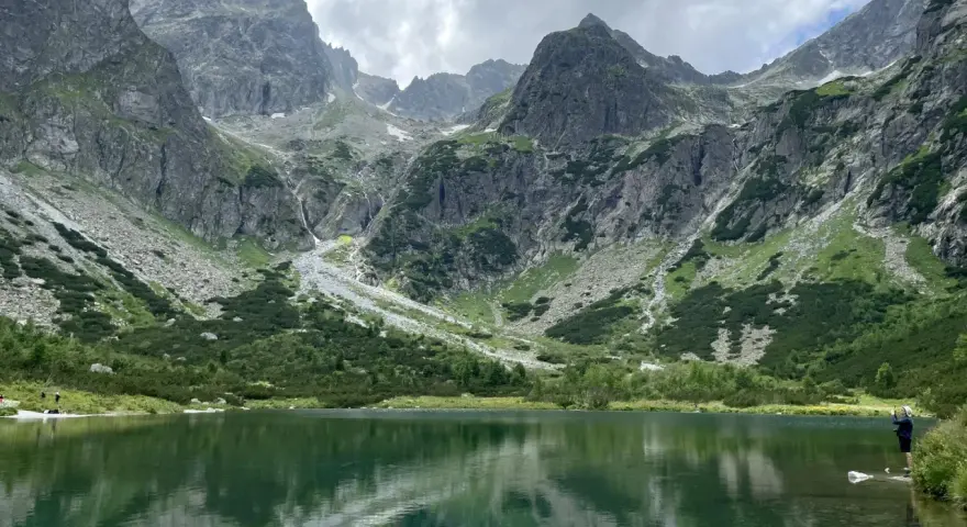 Piękne szlaki na Słowacji. Jezioro w górach odbija skaliste szczyty i zielone zbocza.