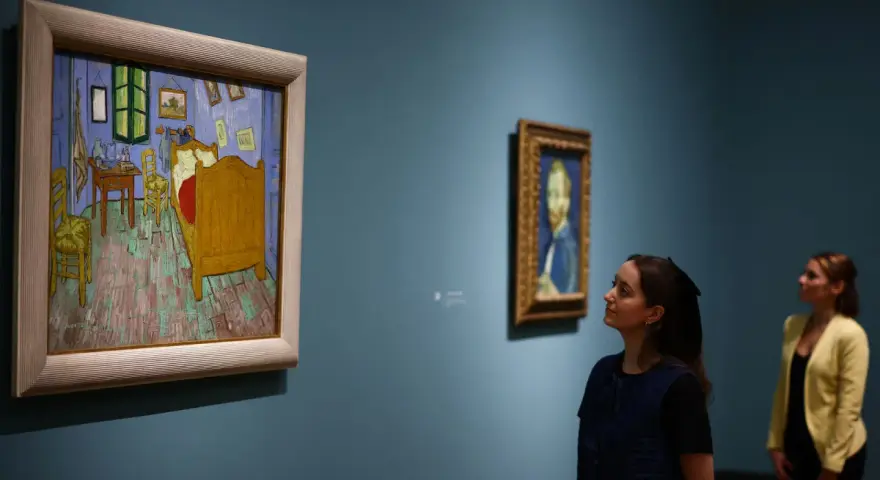 Deux femmes contemplent des tableaux. À gauche, la chambre de Van Gogh, une œuvre iconique dont le prix tableau peinture à l'huile fascine.