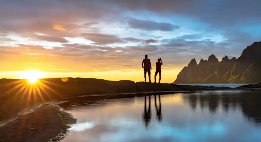 Två silhuetter står på en klippa vid havet och ser på solnedgången över Bodo, Norge. Bergskedja i bakgrunden.