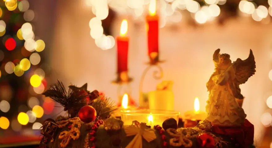 Ein Adventskranz mit Kerzen und einem Engel, umgeben von Weihnachtsbaumlichtern.
