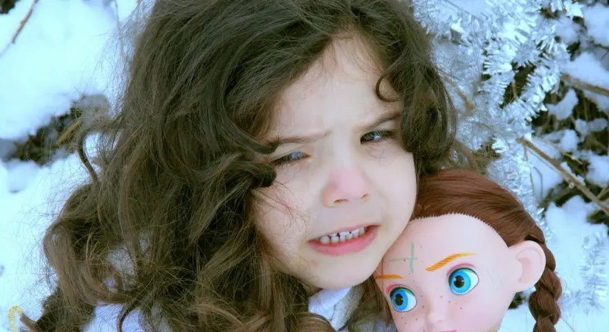 Ein Kind mit dunklen Haaren hält eine Puppe im Schnee. Das Kind sieht besorgt aus, als ob mein Kind Angst vor mir hätte.
