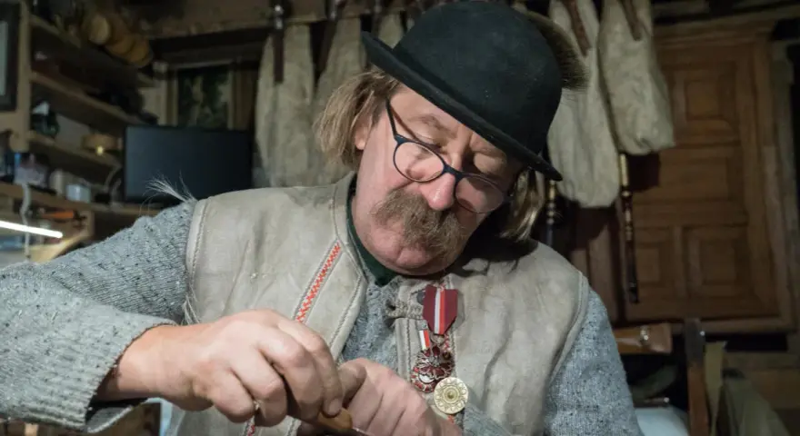 Piotr Majerczyk, z siwym dymem w tle, skupiony na pracy, w kapeluszu i z medalami na piersi.