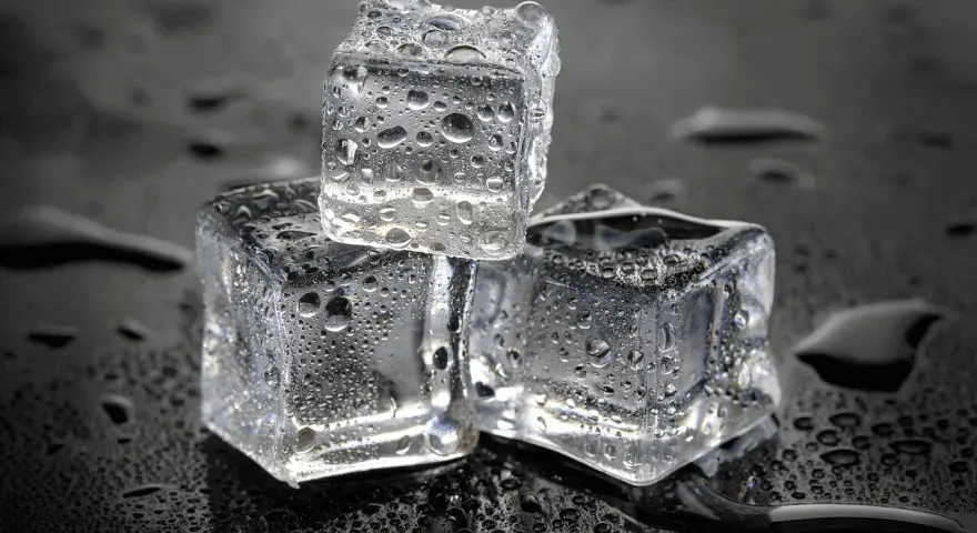 Drei eiswürfel mit Wassertropfen auf schwarzem Hintergrund. Die Frage, wie lange braucht Eis zum Gefrieren, wird hier visuell beantwortet.