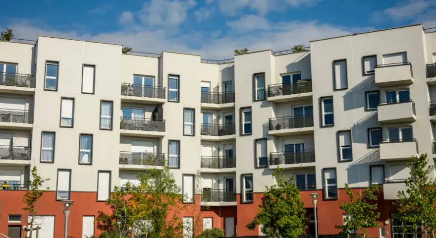 Immeuble moderne aux balcons noirs, un **idéal de la loge** avec ses façades blanches et sa base rouge. Ciel bleu et nuages.