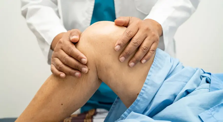 Fizjoterapeuta delikatnie masuje kolano pacjenta w niebieskiej koszuli.