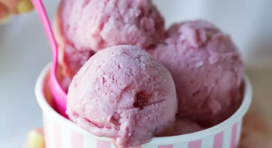 Różowe lody w kubeczku, z różową łyżeczką. Zastanawiasz się, ile kalorii mają lody?