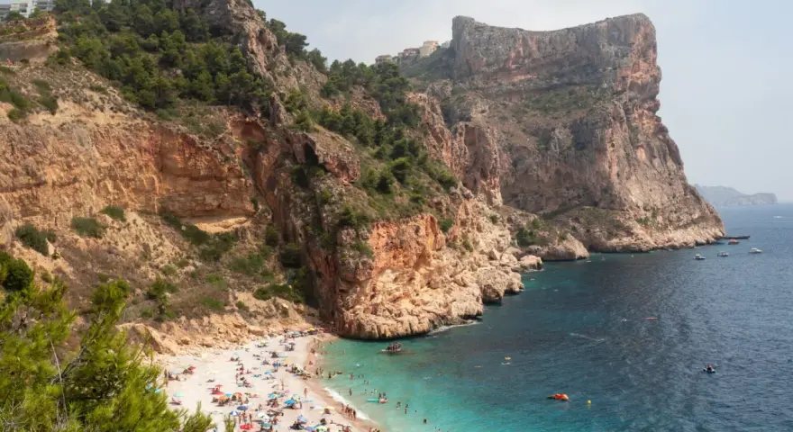 Playa con acantilados y gente disfrutando del sol y el mar. Un plan perfecto para saber qué ver en Alicante provincia en una semana.