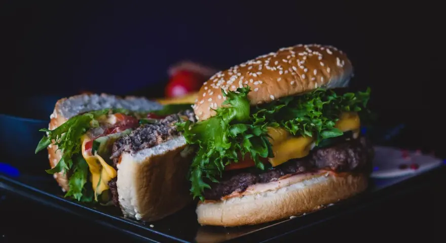 Dwa soczyste burgery z serem, sałatą i warzywami na ciemnym tle.