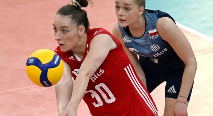 Siatkarka w czerwonej koszulce odbija piłkę, druga zawodniczka w niebieskiej koszulce obserwuje grę. Emocjonujące mecze siatkówki.
