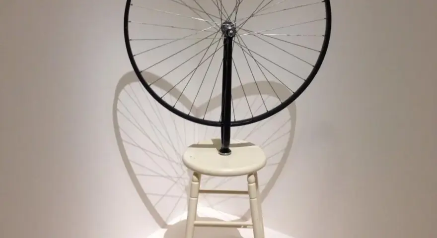 Roue de vélo fixée sur un tabouret, une œuvre emblématique de Marcel Duchamp, projetant une ombre fascinante.