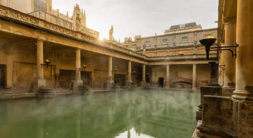 Steaming green water fills the Great Bath, surrounded by ancient Roman ruins with columns and torches.