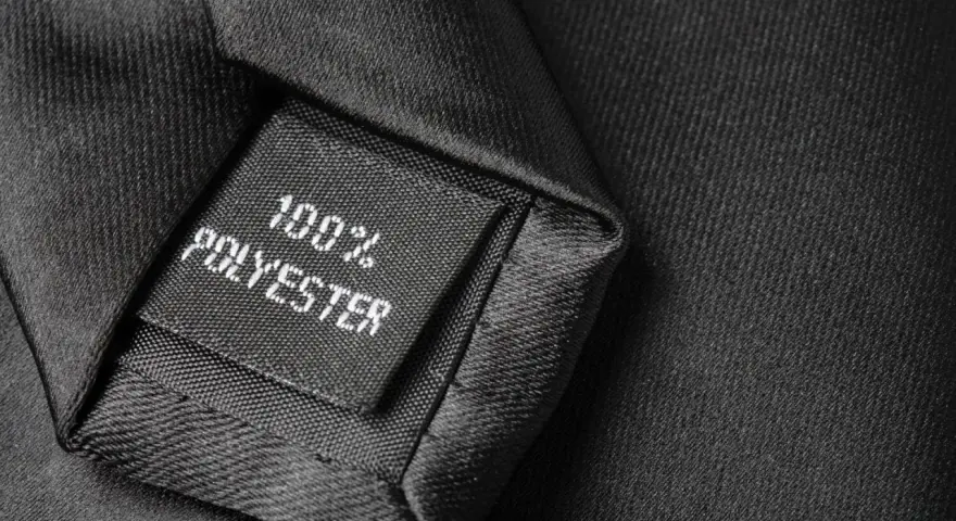 Czarna metka z napisem "100% POLYESTER" na tle eleganckiego materiału. Czy poliester to dobry materiał?