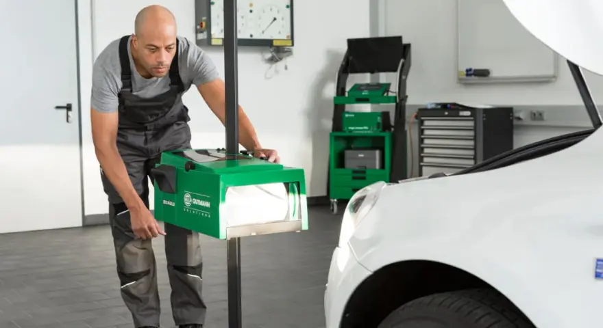 Mechanik dokonuje ręcznej regulacji świateł samochodu za pomocą zielonego urządzenia.
