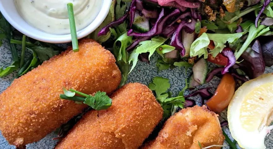Croquetas doradas y crujientes con ensalada fresca, salsa y limón.