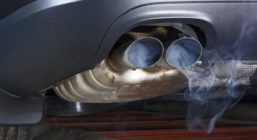 Dwa końcówki wydechu samochodu z wydobywającym się dymem, sugerujące czyszczenie katalizatora.