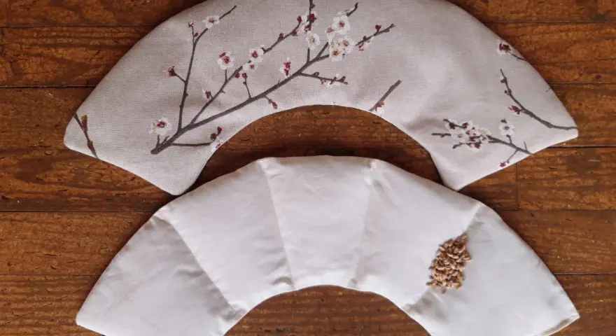 Tuto bouillotte sèche cervicale : deux coussins en tissu, l'un décoré de fleurs de cerisier, l'autre prêt à être rempli de grains.