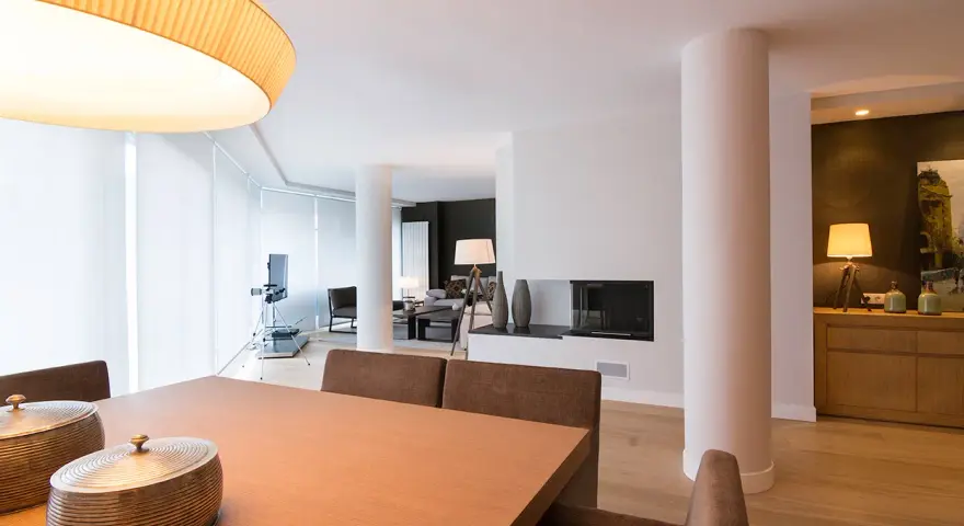 Comedor y salón modernos tras reforma piso pequeño. Mesa de madera, chimenea y mobiliario elegante.