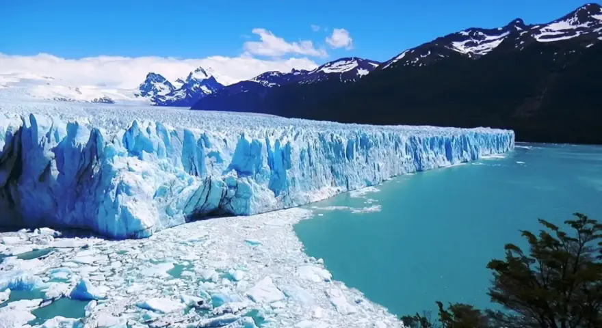 Impresionante glaciar Perito Moreno, con sus paredes de hielo azul intenso y el agua turquesa del lago. Montañas nevadas al fondo.