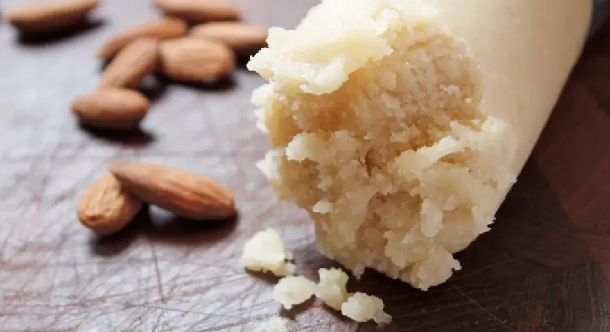 Frische Mandeln liegen neben einer Rolle Marzipan Rohmasse, bereit zum Verarbeiten.