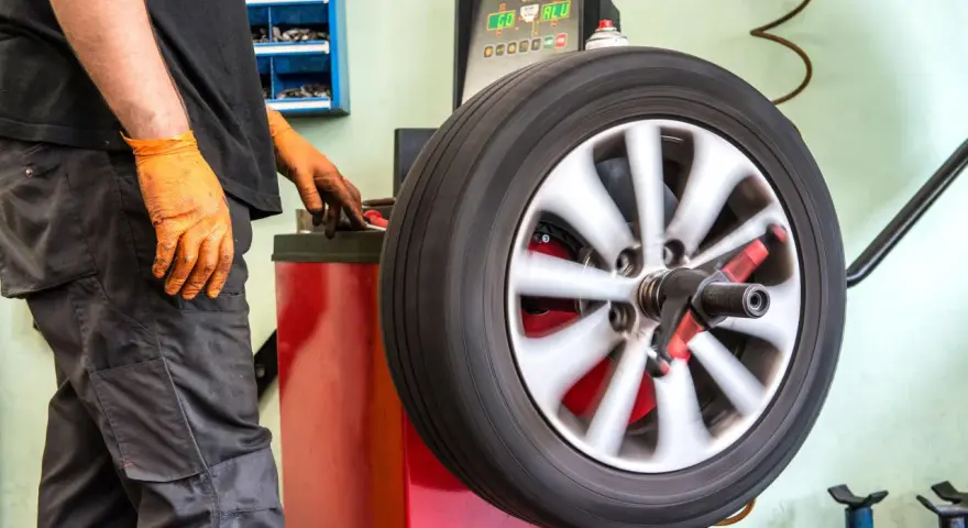 Meccanico con guanti arancioni controlla la vibrazione auto semiasse su una macchina bilanciatrice.