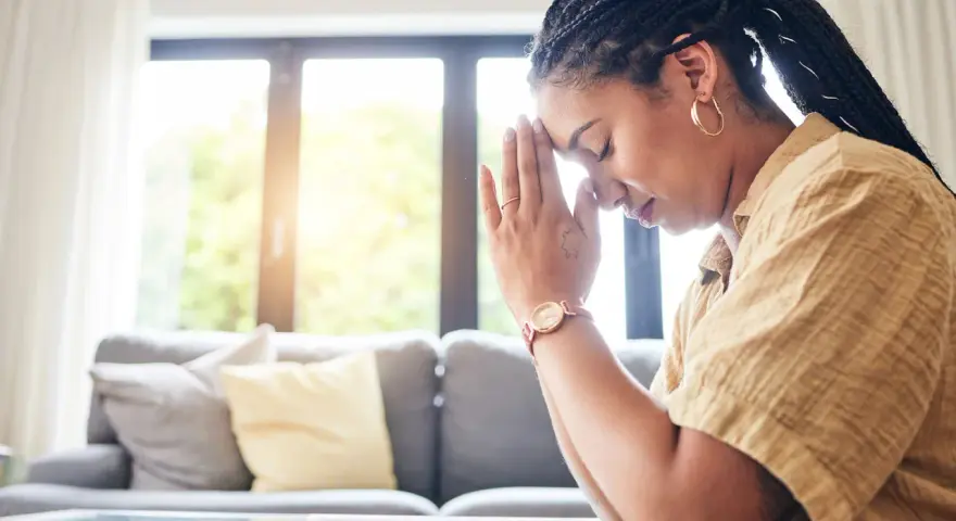 A woman with braided hair and hoop earrings prays with her hands clasped, finding peace during her christian prayer times.