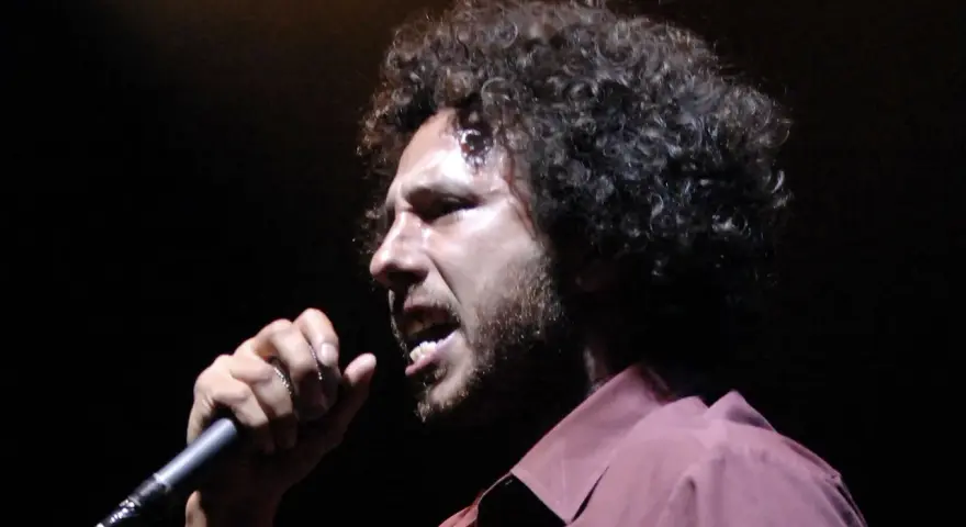 Zack de la Rocha heute, mit seinem charakteristischen lockigen Haar und einem Mikrofon in der Hand, singt leidenschaftlich auf der Bühne.