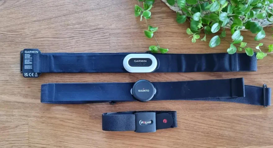 Tre pulsbands från Garmin, Suunto och Polar ligger på ett trägolv. Jämför garmin pulsband skillnad med de andra.