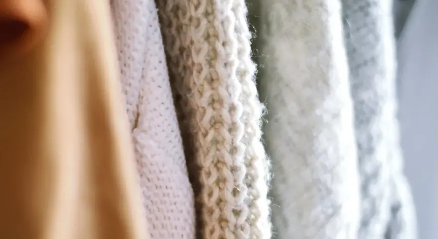 Nahaufnahme von Strickwaren in verschiedenen Pastelltönen. Die feine Struktur zeigt, dass Merinowolle fusselt, was den weichen Charakter unterstreicht.